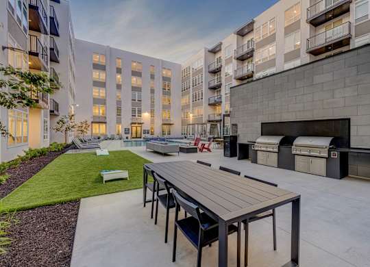 A modern outdoor seating area with a long table and chairs is surrounded by apartment buildings.