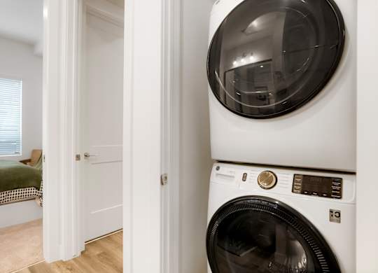 A white washing machine in a room with a bed in the background.