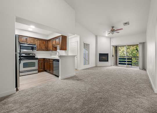 A spacious living room with a ceiling fan and a sliding glass door leading to a balcony.