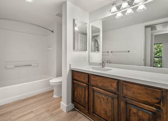 A white bathroom with wooden cabinets and a large mirror.