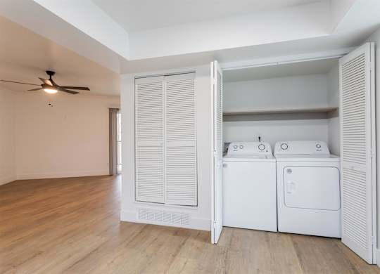 A room with a white wall and a white floor with a white washing machine and dryer in it.