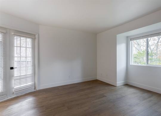A room with white walls and wooden flooring, with a window on the right side.
