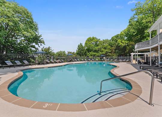 A large outdoor swimming pool surrounded by trees and lounge chairs.