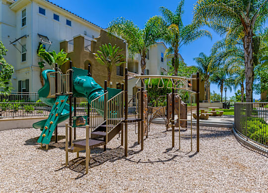 A playground with a green slide and a brown swing set.