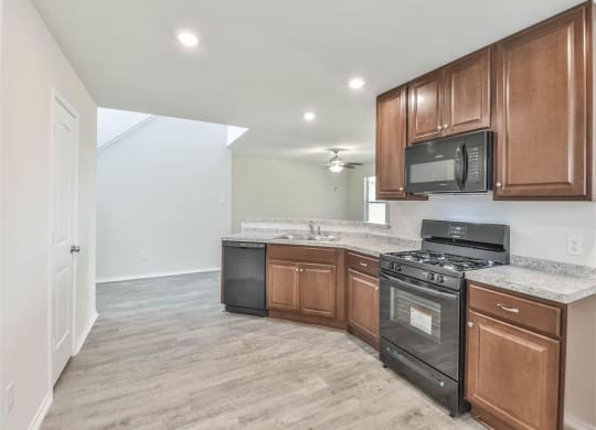 an empty kitchen with wood cabinets and black appliances at The Village at Caney Mills, Conroe