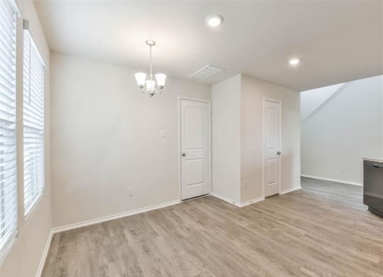an empty living room with white walls and wood flooring at The Village at Caney Mills, Conroe