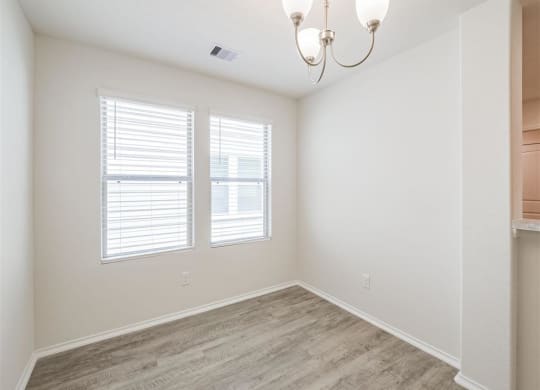an empty room with two windows and a chandelier at The Village at Caney Mills, Conroe, TX