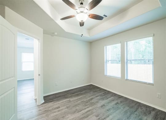an empty living room with a ceiling fan and two windows at The Village at Caney Mills, Conroe, Texas