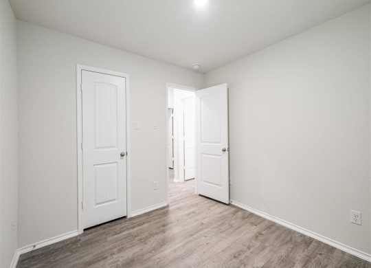 an empty living room with white walls and wood floors at The Village at Caney Mills, Conroe, TX