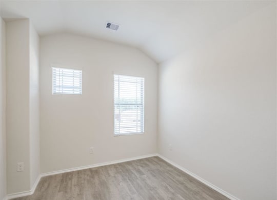 an empty room with white walls and wood floors at The Village at Caney Mills, Conroe, TX