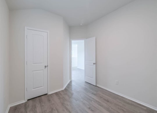 a bedroom with white walls and doors and a wood floor at The Village at Caney Mills, Conroe, TX