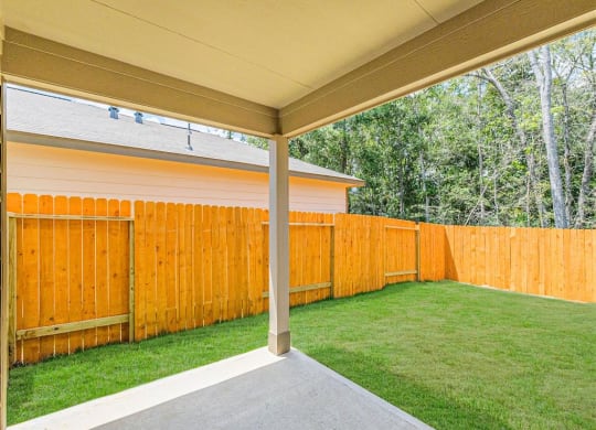 a covered patio with a lawn and a wooden fence at The Village at Caney Mills, Conroe