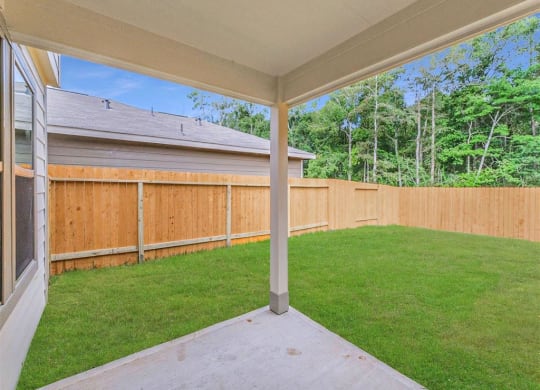 a backyard with a wooden fence and a patio with grass at The Village at Caney Mills, Conroe, 77303