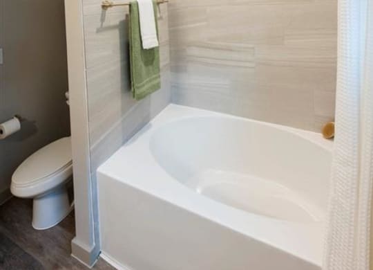 a bathroom with a white tub and a toilet and a green towel
