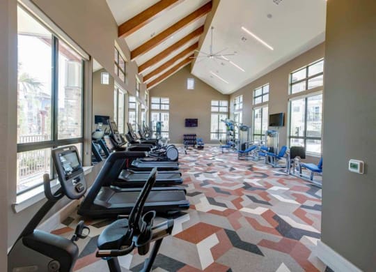 a gym with cardio equipment and large windows