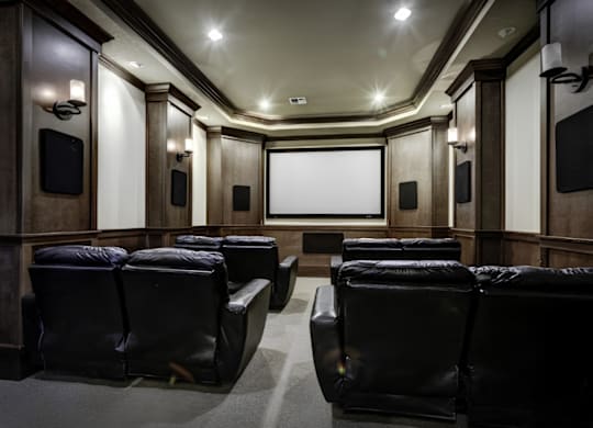 A dark cinema room with black leather seats and a screen at the front.