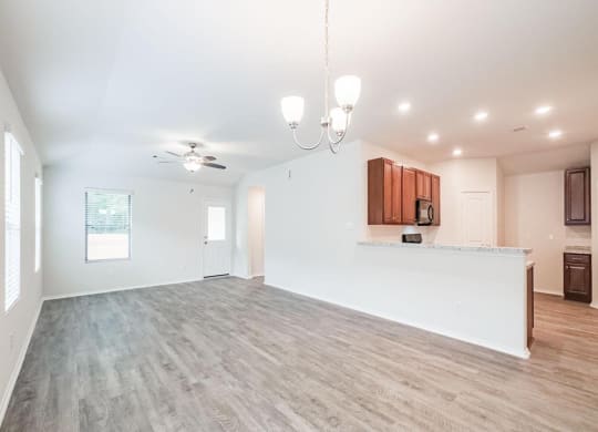 an empty living room with a kitchen and a ceiling fan