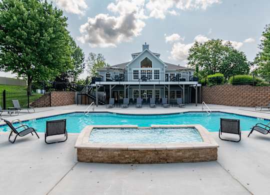 A pool with a hot tub and a house in the background.