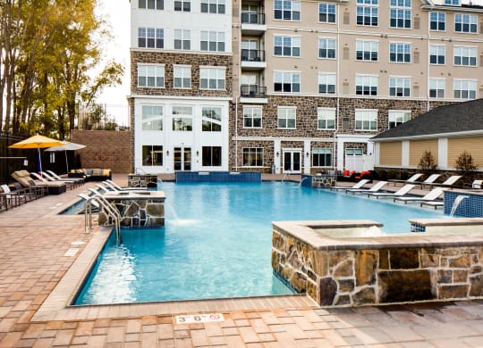 a pool with a stone wall and lounge chairs in front of a building at Heights at Glen Mills, Glen Mills