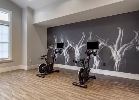 a home gym with two exercise bikes in front of a wall with art on it at Reserve by the Lake, Houston, Texas