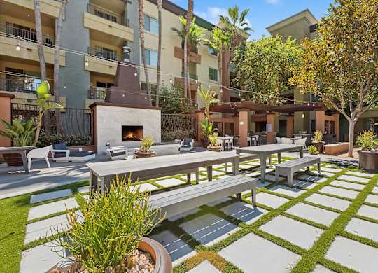 A patio with a table and chairs is surrounded by a grassy area and apartment buildings at The Kitt at Warner Center Apartments, California, 91303
