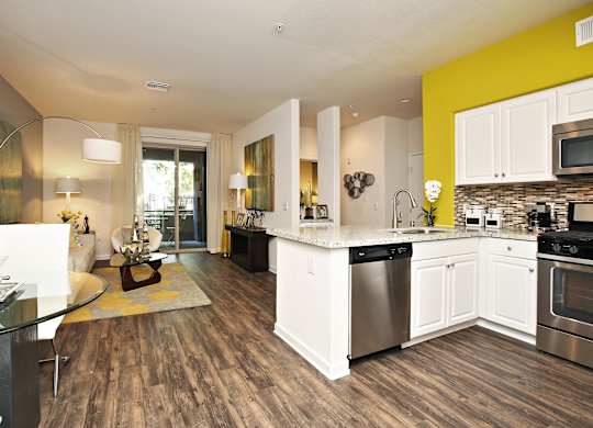 A modern kitchen with white cabinets and a wooden floor at The Kitt at Warner Center Apartments, Woodland Hills