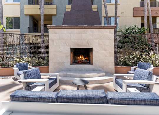 A fireplace is in the middle of a patio with blue cushioned chairs around it at The Kitt at Warner Center Apartments, California, 91303
