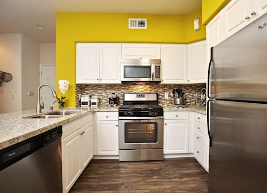 A kitchen with a yellow wall and stainless steel appliances at The Kitt at Warner Center Apartments, California, 91303