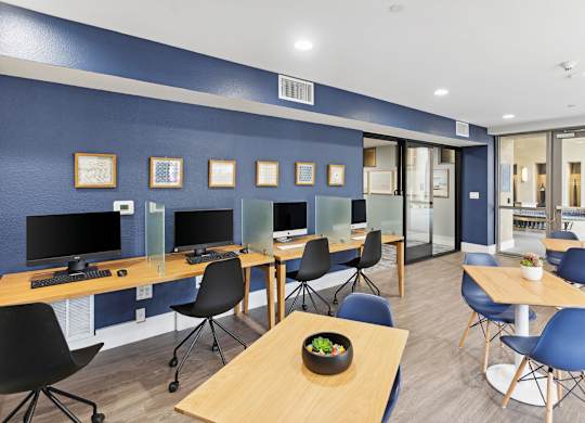 A room with blue walls and wooden tables with chairs at The Kitt at Warner Center Apartments, Woodland Hills, CA