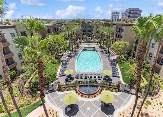 A pool surrounded by palm trees and umbrellas at The Kitt at Warner Center Apartments, Woodland Hills 91303