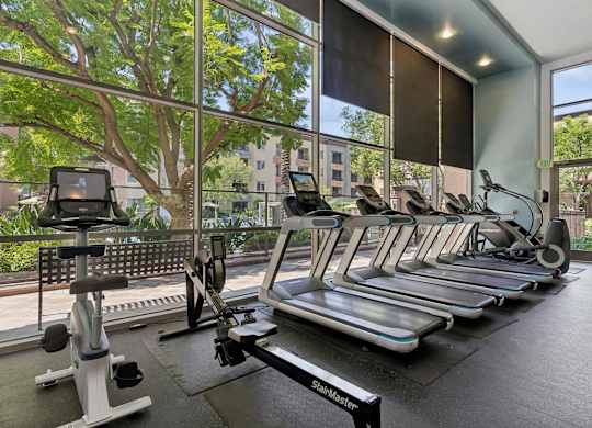 A gym with treadmills, elliptical machines, and a rowing machine at The Kitt at Warner Center Apartments, Woodland Hills, CA, 91303