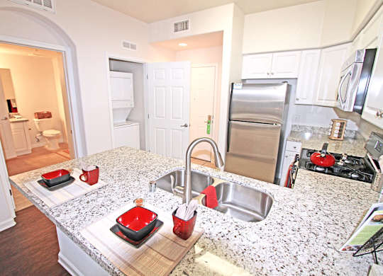 A kitchen with a granite counter top and stainless steel appliances at The Kitt at Warner Center Apartments, Woodland Hills 91303