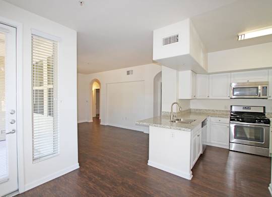 A kitchen with white cabinets and a wooden floor at The Kitt at Warner Center Apartments, Woodland Hills