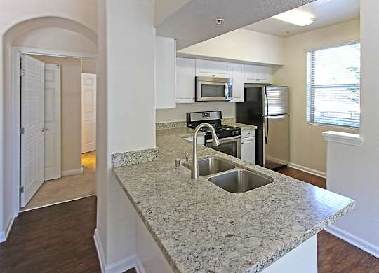 A kitchen with granite countertops and stainless steel appliances at The Kitt at Warner Center Apartments, Woodland Hills, California