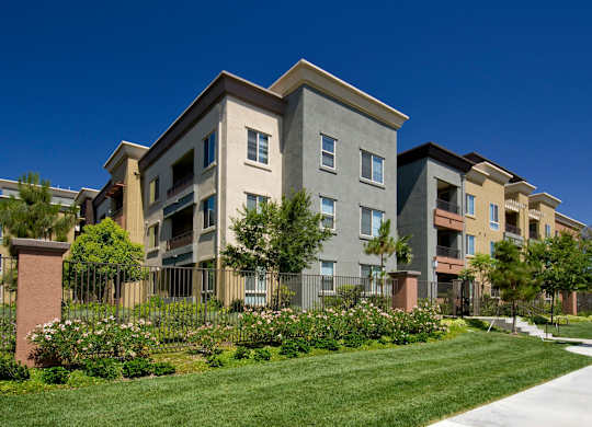 A row of modern apartment buildings with a well-maintained lawn in front. at The Kitt at Warner Center Apartments, California