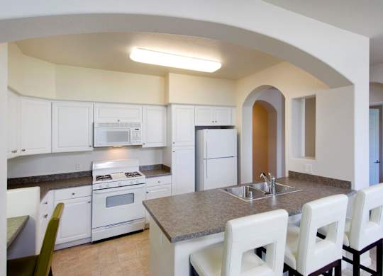 A kitchen with white cabinets and a countertop with a sink and four chairs at The Kitt at Warner Center Apartments, California