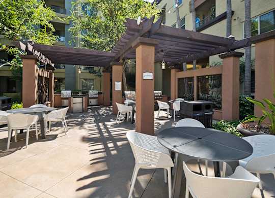 A patio with tables and chairs under a pergola. at The Kitt at Warner Center Apartments, Woodland Hills, CA, 91303
