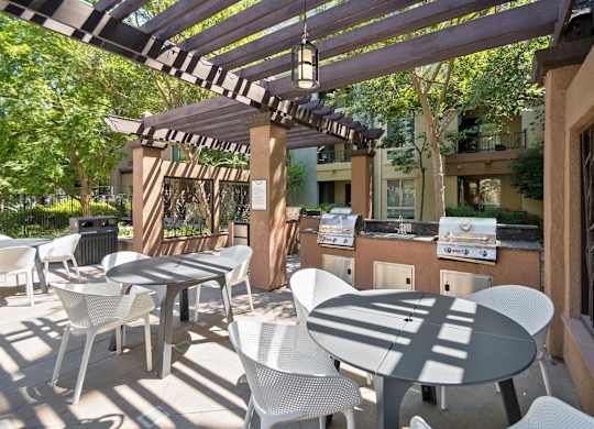 A patio with white chairs and tables is covered by a striped awning at The Kitt at Warner Center Apartments, Woodland Hills, CA, 91303