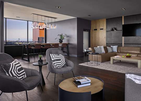 A modern living room with a grey couch, a wooden coffee table, and a large window overlooking the city.