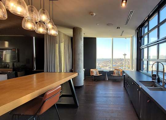 A modern kitchen with a long wooden table and a view of the city.
