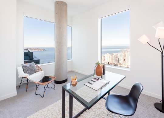 A modern dining room with a glass table and chairs, a floor lamp, and a view of the city and water.
