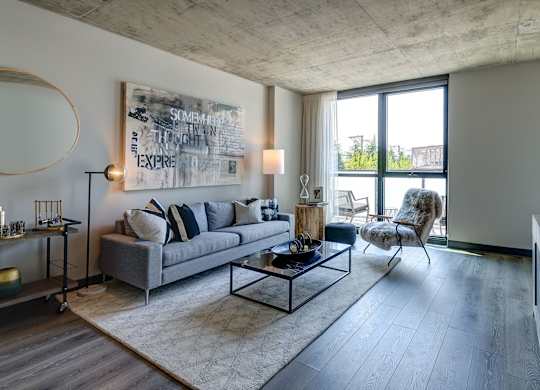 A modern living room with a grey sofa, a coffee table, and a large abstract painting on the wall. at The Mason Apartments, Chicago, IL