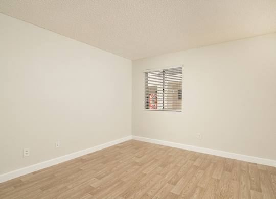 A room with wooden flooring and a window with blinds.