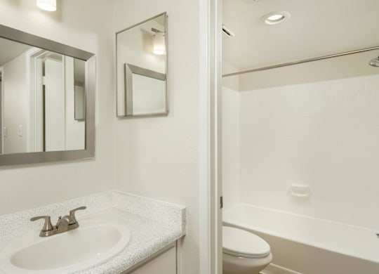 A white bathroom with a sink, mirror, toilet and bathtub.