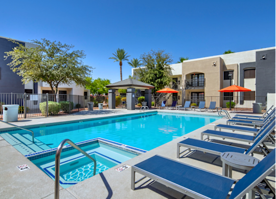 A swimming pool with sun loungers and umbrellas in front of a building.
