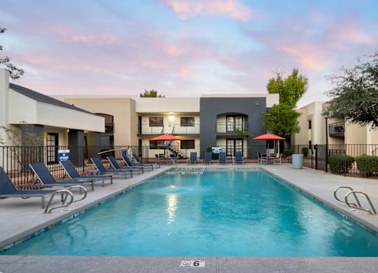 A swimming pool surrounded by lounge chairs and a building in the background.