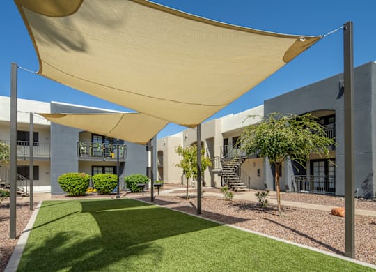 A sunny day at a modern apartment complex with a green lawn and a shade sail.