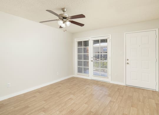 A room with a ceiling fan and sliding glass doors.