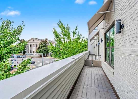 A balcony with a white railing overlooks a street with cars and buildings.