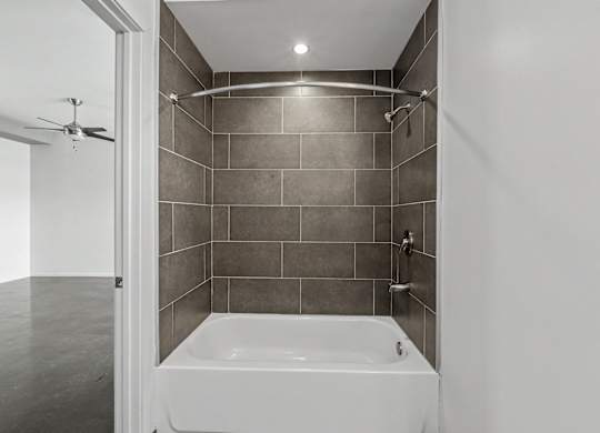 A white bathtub is in a bathroom with grey tiles.